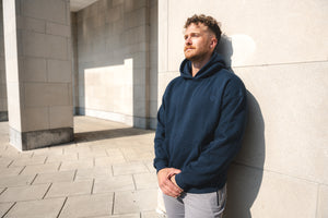 Man wearing a Cadet Foundation Barbell hoodie standing against a light-colored wall.