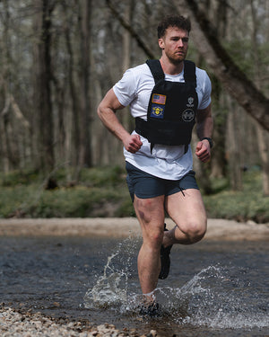 Model wearing Barbell Havok Tee and Charcoal Rapid Hybrid Shorts running through creek