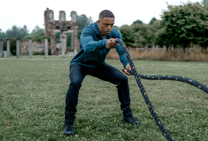 Man in barbell jeans and hoodie with battle ropes