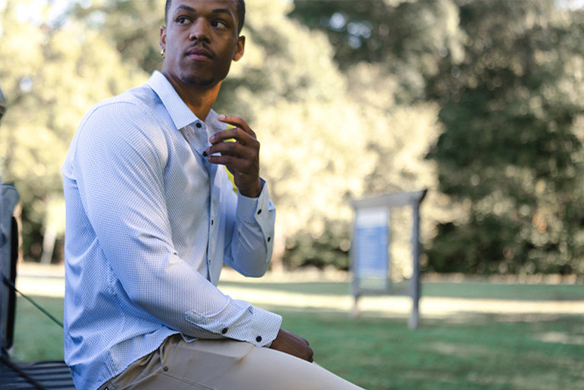 Man sitting outdoors in a park wearing a long sleeve motive dress shirt