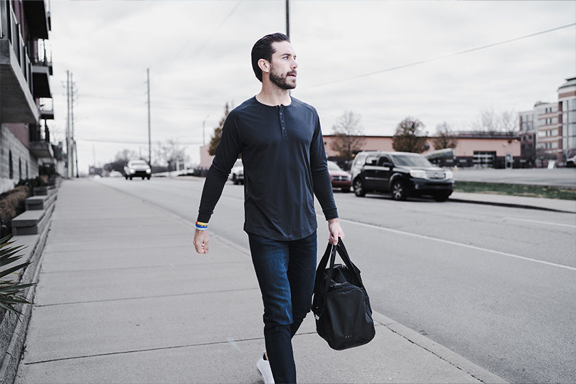 Man walking on a sidewalk holding a black bag in an urban setting Wearing Barbell Scout Henley