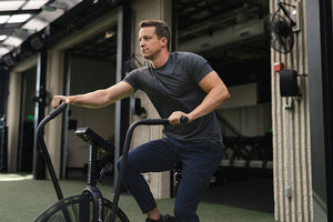 Man exercising on a stationary bike in an indoor setting in Ultralight Tech Tee and adapt joggers