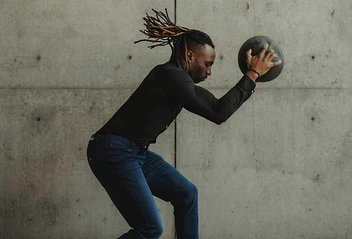 Person in motion with a medicine ball against a concrete wall.