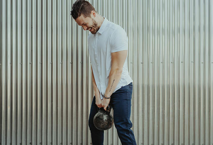 Man smiling while holding a kettlebell in front of a metal wall.